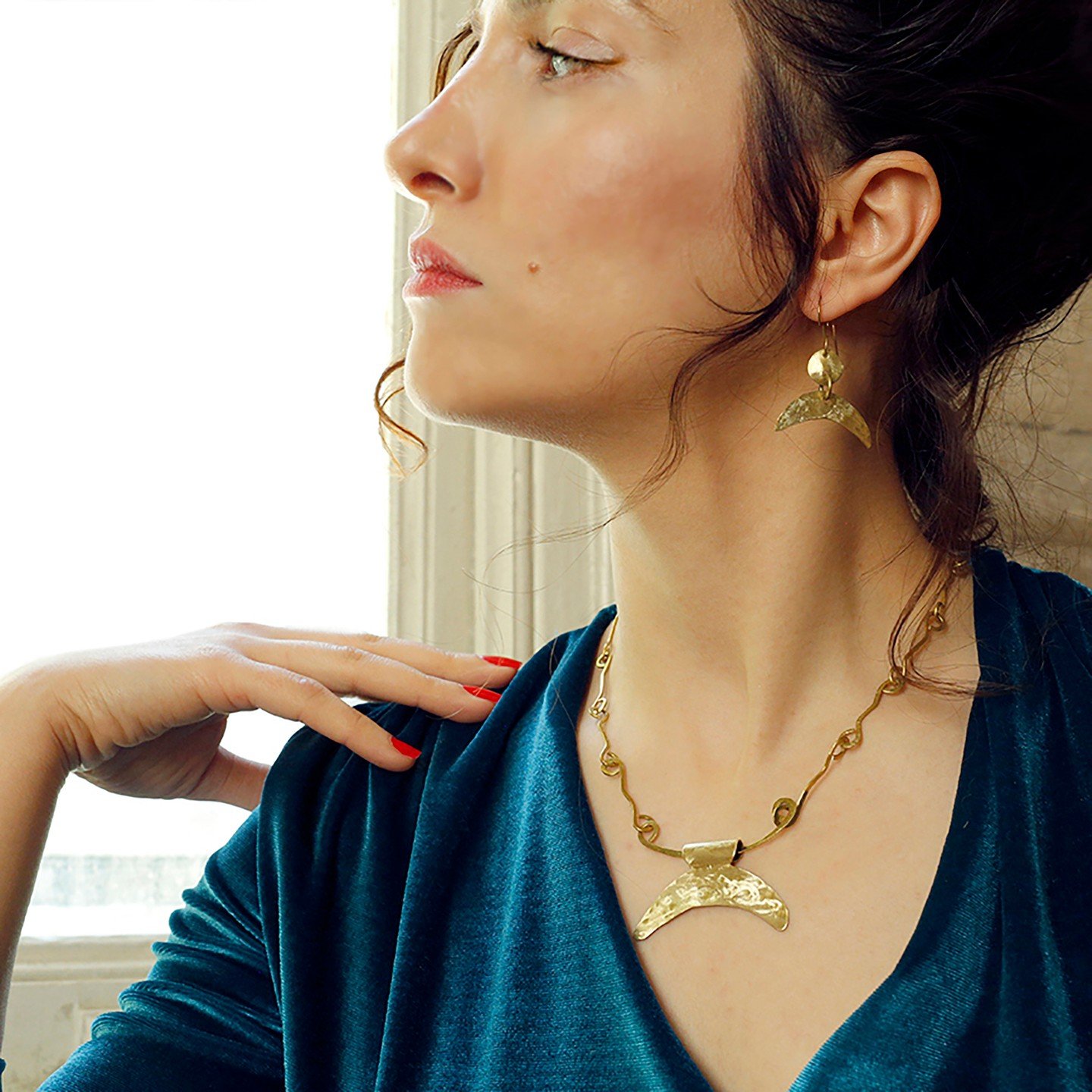 Model wearing a crescent pendant and earrings beside a bright window